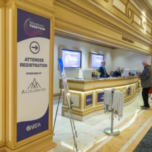 People stand at a registration desk in a convention center lobby, with signage for "Attendee Registration" sponsored by Accelerated.