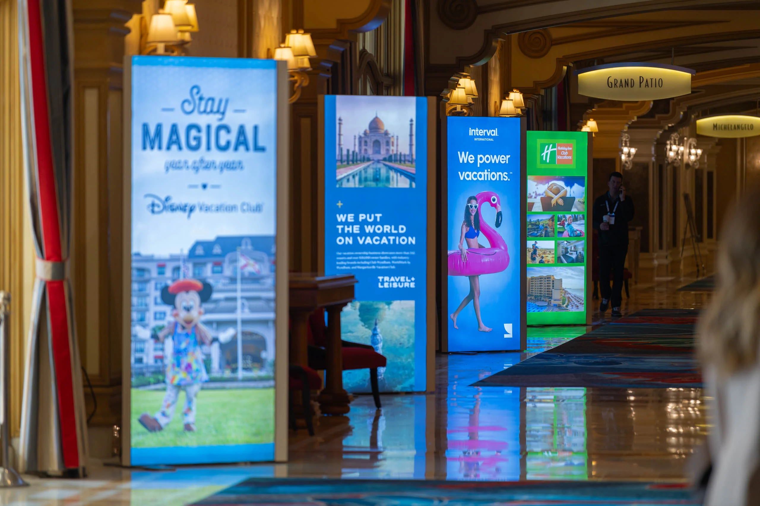 A hallway with illuminated vacation advertisement signs, featuring themes like Disney, travel destinations, and vacation rental services.